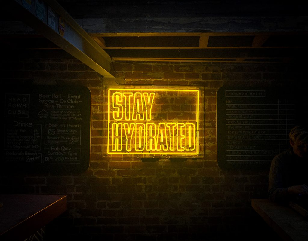 Image of a neon sign that reads, "Stay Hydrated" lit against a brick wall.