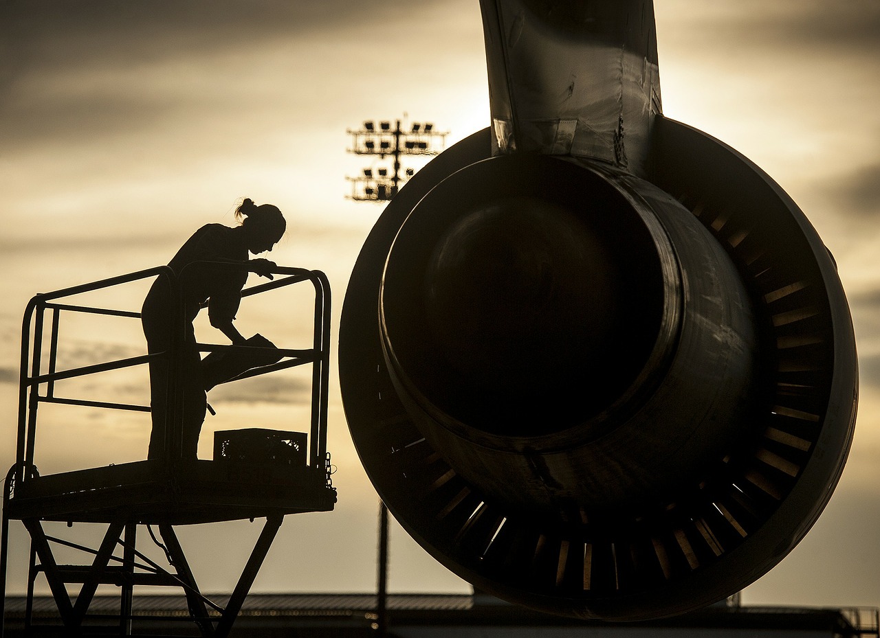 Image of an aircraft mechanic on a lift near an engine at sunset