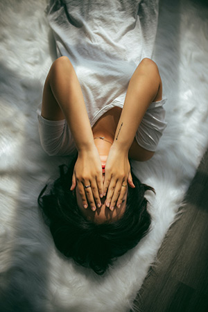 Image of a woman laying on the floor with her hands over her face.