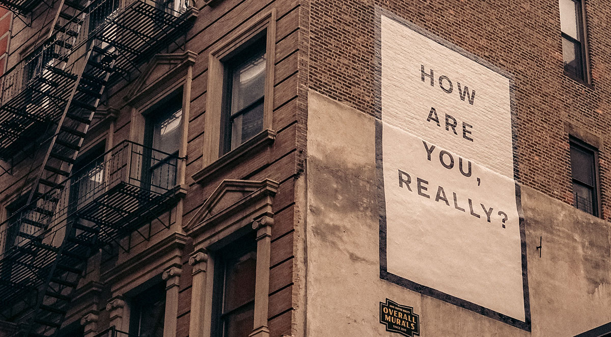Image of a brown brick multi-story building with "How are you, Really?" painted on the side.